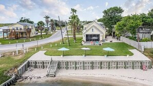 A waterfront property with a grassy deck, a small building with a porch, and a wooden dock extending into the water. - We Dig It at Magnolia Beach Texas (Port Lavaca)