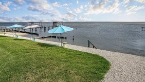 A waterfront property with a dock, umbrellas, and a grassy area. - We Dig It at Magnolia Beach Texas (Port Lavaca)