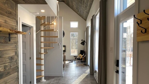 A modern interior with a wooden staircase, a dining area, and a view of the outdoors.