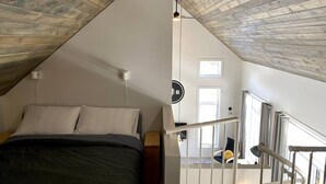 A bedroom with a sloped ceiling, a bed, a chair, and a staircase.