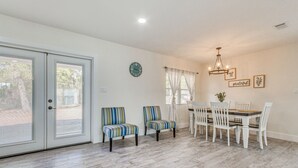 Un comedor con una mesa y sillas blancas, un reloj en la pared y una ventana con cortinas.