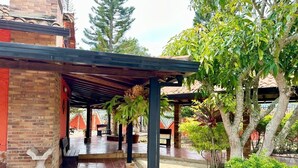 A covered outdoor area with tiled flooring, wooden benches, and a stone sculpture. - Hotel Cristo Rey Campestre (Los Santos)