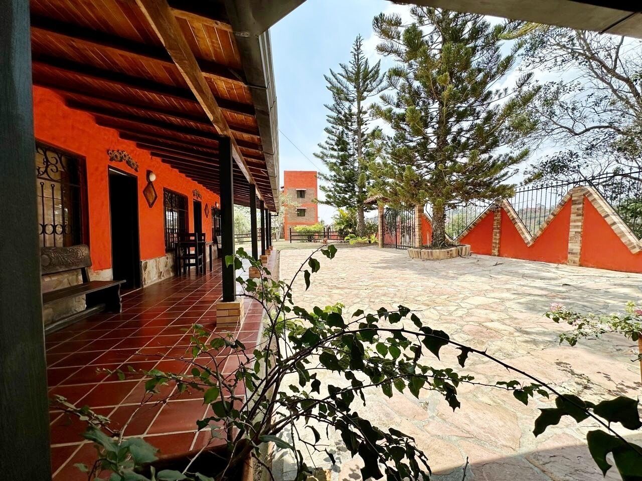 Ein Außenbereich mit einer Terrasse, rotem Fliesenbelag, einer Holzw pergola und Blick auf ein Gebäude im Hintergrund.