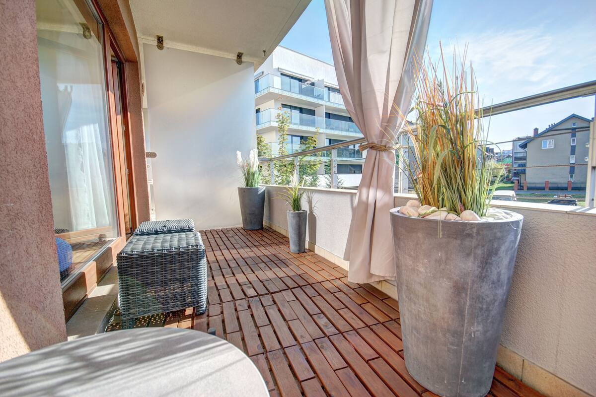 A balcony with a wooden floor, potted plants, and a view of buildings.