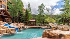 Un espace piscine doté d’un toboggan aquatique, d’un kiosque et offrant une vue sur un paysage montagneux.