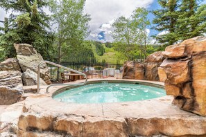 A hot tub surrounded by rocks and trees, with a view of a forested hillside.