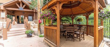 Ein hölzerner Pavillon mit Tisch und Stühlen, umgeben von einem Kiesweg und einem Holzzaun.