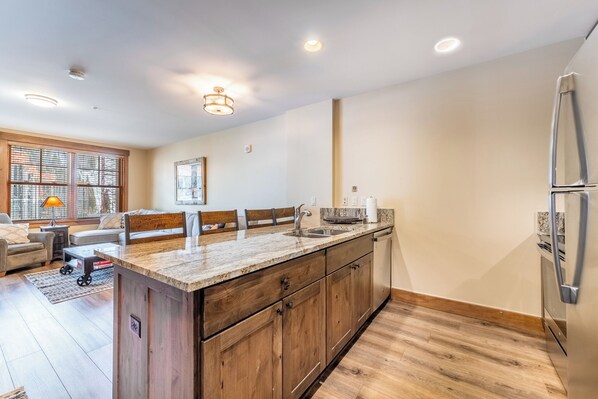 A modern kitchen with wooden cabinets, a marble countertop, and a stainless steel refrigerator. - Springs #8875 By Summit County Mountain Retreats (Keystone)