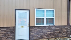A building with a white door, a window with blinds, and a stone facade. - Breckenridge Suites #6 - Cozy 1-Bedroom Suite with Fully Equipped Kitchen (Grove City)
