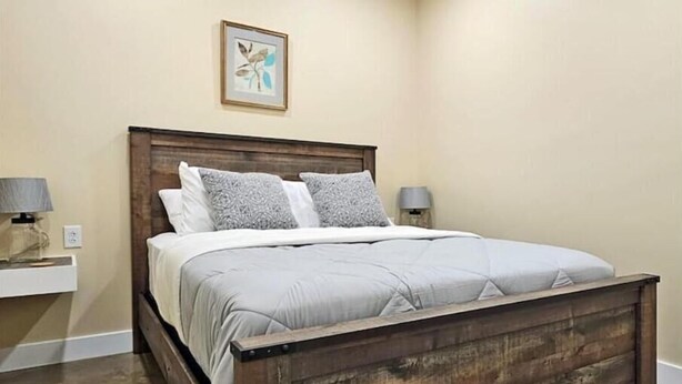 A bedroom with a wooden bed frame, white bedding, and two bedside lamps. - Breckenridge Suites #6 - Cozy 1-Bedroom Suite with Fully Equipped Kitchen (Grove City)