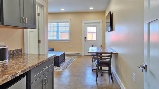 A kitchen with dark cabinets, a granite countertop, and a dining area with a table and chairs. - Breckenridge Suites #2 - One-Bedroom Suite Perfect for Business or Leisure (Grove City)
