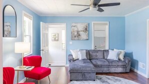 A living room with a grey sectional sofa, red armchairs, a ceiling fan, and artwork on the walls. - Private Hudson Valley Escape (Kingston)