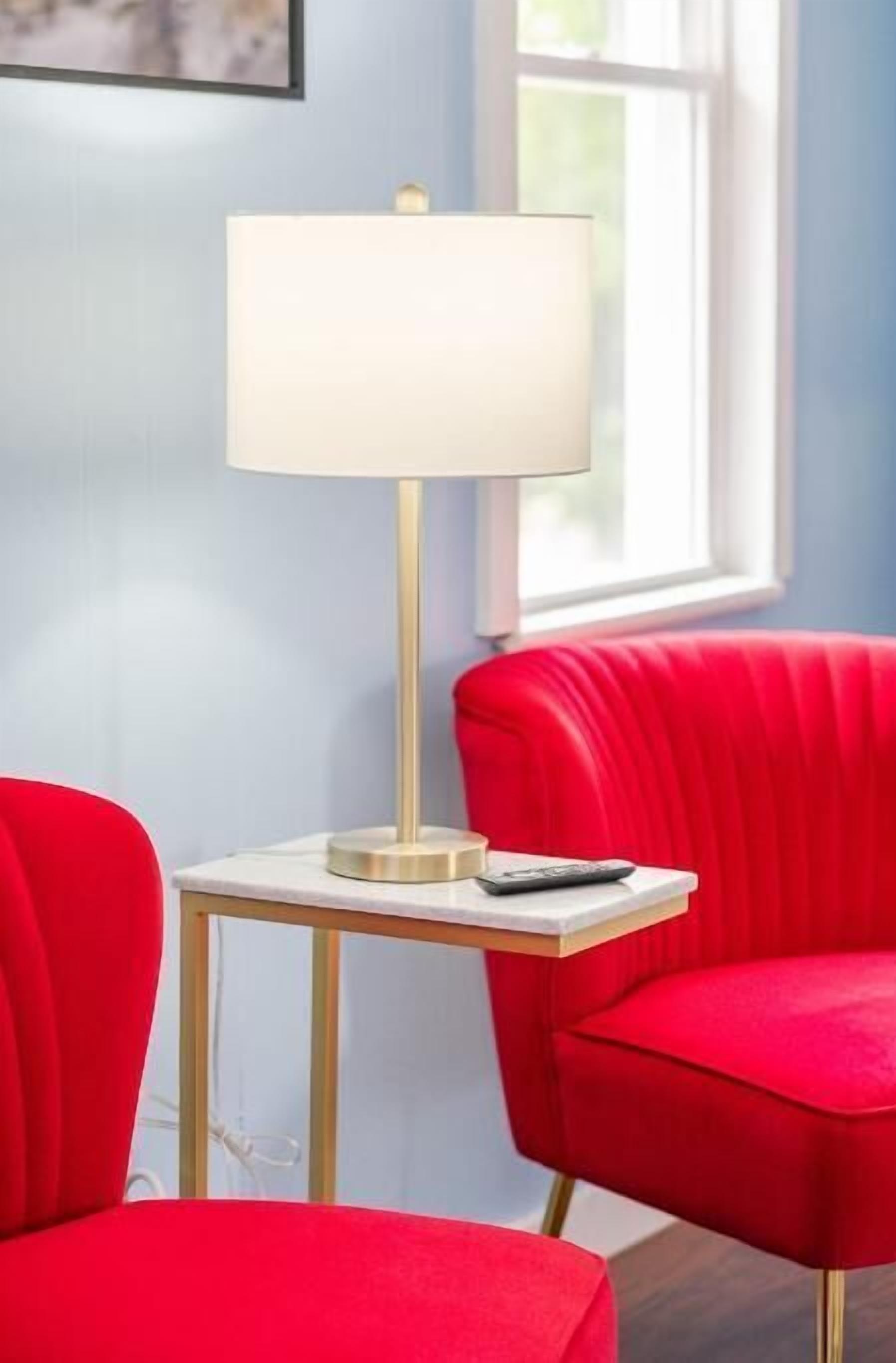 Une pièce moderne avec un lampadaire blanc sur une petite table, des chaises à revêtement rouge et une fenêtre laissant entrer la lumière naturelle.