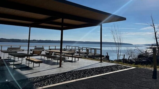 An outdoor seating area with tables and benches, a covered pavilion, and a view of a lake and distant landforms. - Private Hudson Valley Escape (Kingston)