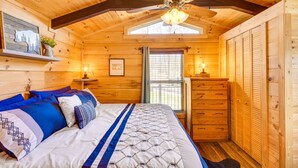 Ein gemütliches Schlafzimmer einer Holzhütte mit Bett, Schminktisch und Deckenventilator.