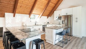 A modern kitchen with a herringbone tile backsplash, wooden ceiling beams, a central island with bar stools, and stainless steel appliances. - Smoky Mountains A-Frame (Sevierville)