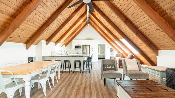 A spacious attic room with a wooden ceiling, a dining table with chairs, a bar area, and a seating area with a sofa and armchairs. - Smoky Mountains A-Frame (Sevierville)
