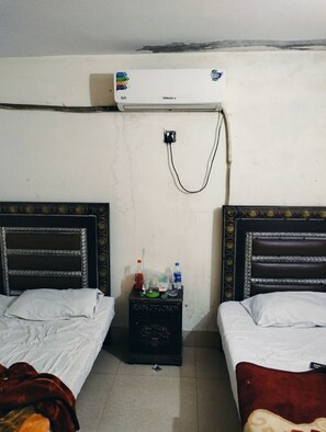 Two single beds with dark headboards and white linens, accompanied by a nightstand and air conditioning unit.