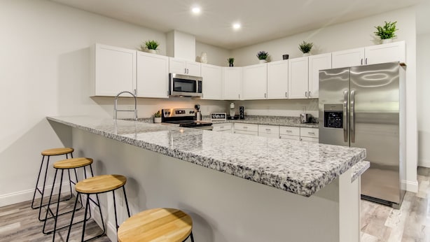 A modern kitchen with white cabinets, a stainless steel refrigerator, a granite countertop, and bar stools. - The Rosezena Experience. (Palmetto)