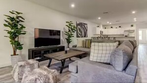A modern living room with a flat-screen TV, a sofa, a coffee table, and two potted plants. - The Rosezena Experience. (Palmetto)
