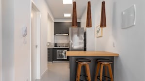A modern kitchen with a central island, two bar stools, pendant lights, and a visible phone on the wall.