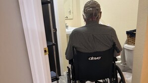 A person in a wheelchair entering a bathroom with a sink and mirror. - Canyon View (Lewiston)