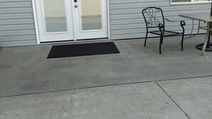 A concrete patio with a black doormat, a metal chair, and a table with a red cloth. - Canyon View (Lewiston)