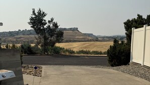A concrete patio with a barbecue grill, a white fence, and a view of distant hills. - Canyon View (Lewiston)