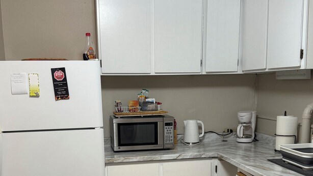 A compact kitchen with white cabinets, a microwave, a coffee maker, and a refrigerator. - Canyon View (Lewiston)