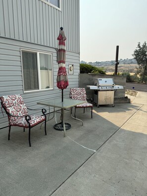 An outdoor patio with a table and chairs, a grill, and a view of the landscape. - Canyon View (Lewiston)
