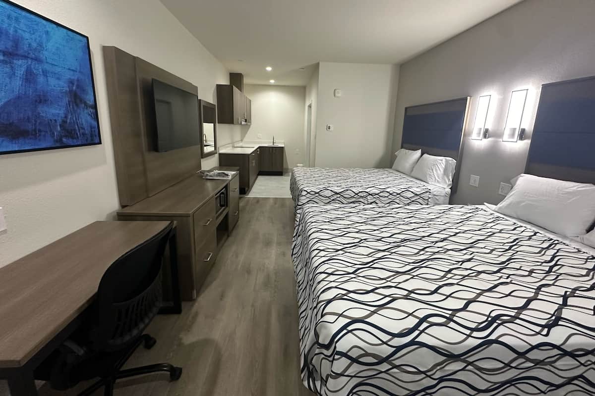 Et hotelværelse med seng, skrivebord, stol og et stort billede på væggen.
