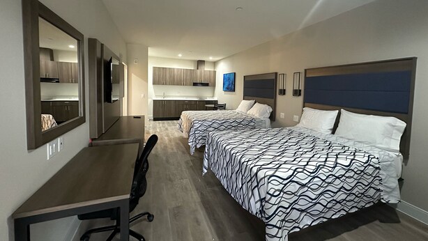 A hotel room with two beds, a desk, a chair, a kitchenette, and a large mirror. - Palace Inn Blue Jones Rd  (Houston)