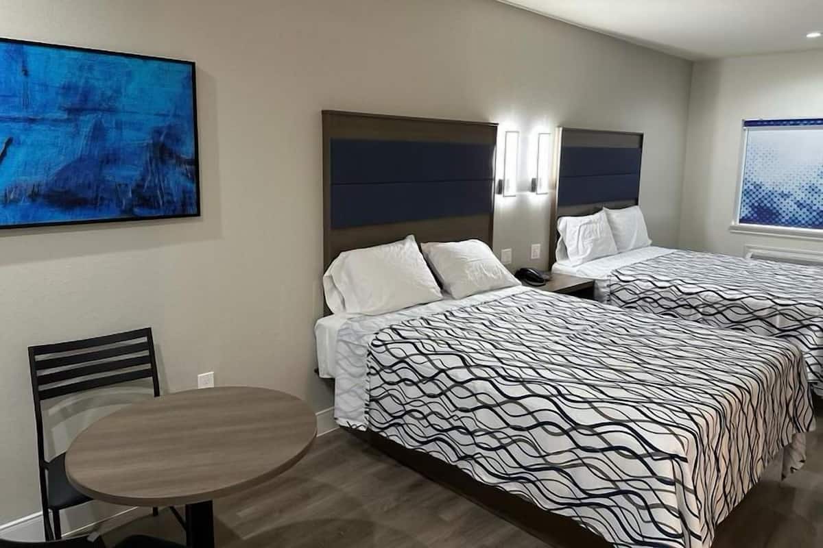 Et hotelværelse med to senge, et spisebord og billedkunst på væggene.