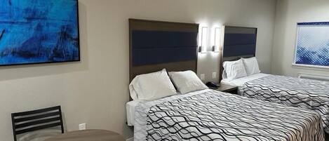 A hotel room with two beds, a dining table, and artwork on the walls.