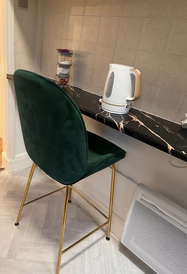 A kitchen with a green chair, a white kettle, and a marble countertop.