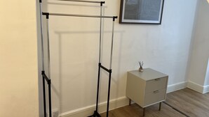 A room with a metal drying rack, a small cabinet, and a framed abstract artwork on the wall. - De Luxe Apartment 1 (Leicester)