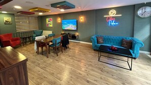 Un salon moderne comprenant un coin repas, un canapé bleu et un panneau lumineux néon sur lequel on peut lire « Café Palace ».