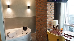 Une salle de bain avec une baignoire blanche, un mur en briques, une table en bois avec une lampe et un téléviseur fixé au mur.