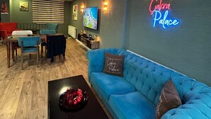 Un salon moderne avec un canapé bleu, une table basse et un panneau lumineux néon sur lequel on peut lire « Calama Palace ».