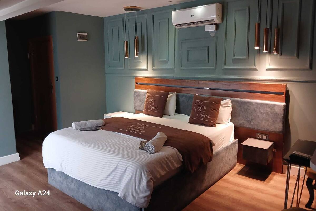 A Galaxy A24 room with a bed, bedside tables, an air conditioning unit, and pendant lights.