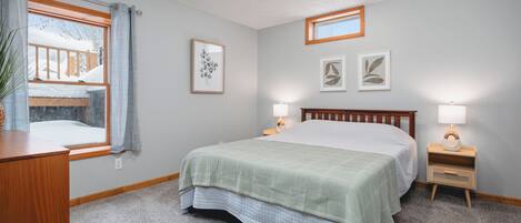 Un dormitorio con cama, lámparas de noche, ventana con cortinas y cuadros en la pared.