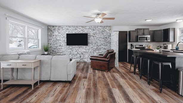 A modern kitchen with a stone backsplash, a flat-screen TV, and a bar area with stools. - Green Lawn (Grawn)