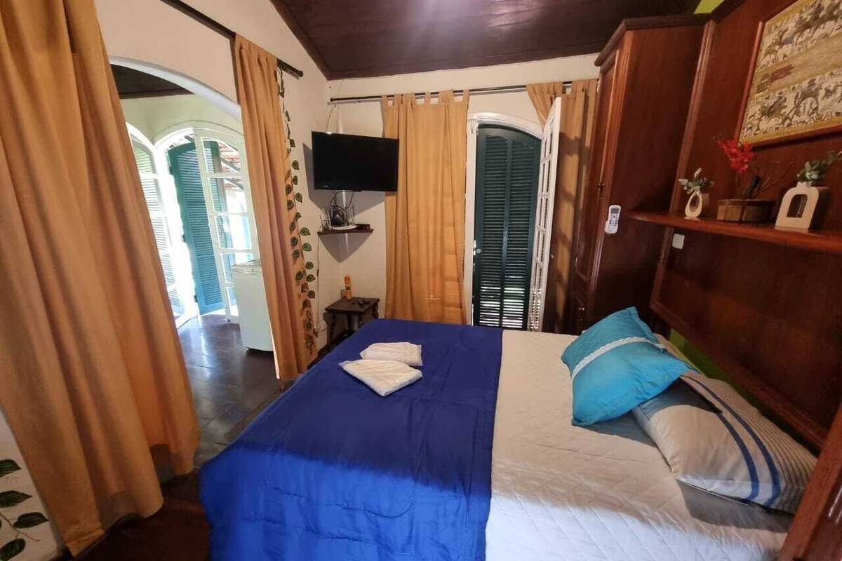 Un dormitorio con cama, cortinas, un televisor y una estantería con adornos.