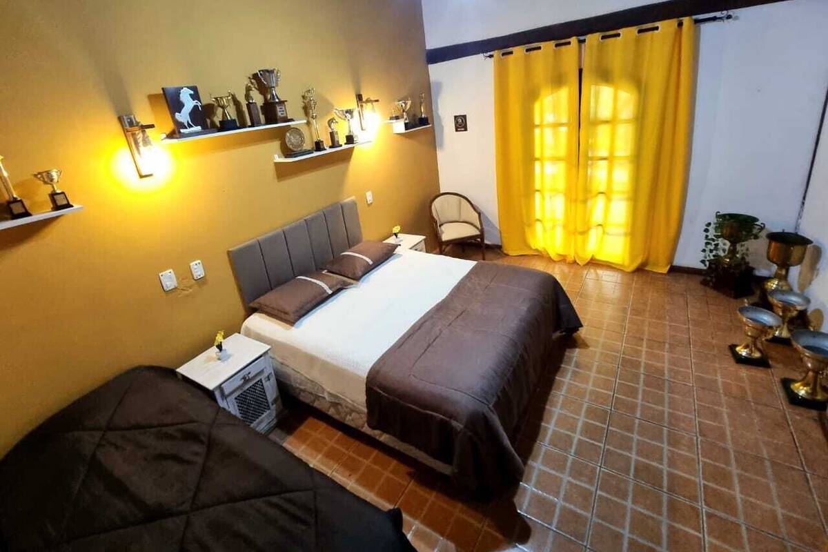 Una habitación con dos camas, un ventilador de techo, una ventana con cortinas amarillas y trofeos en la pared.