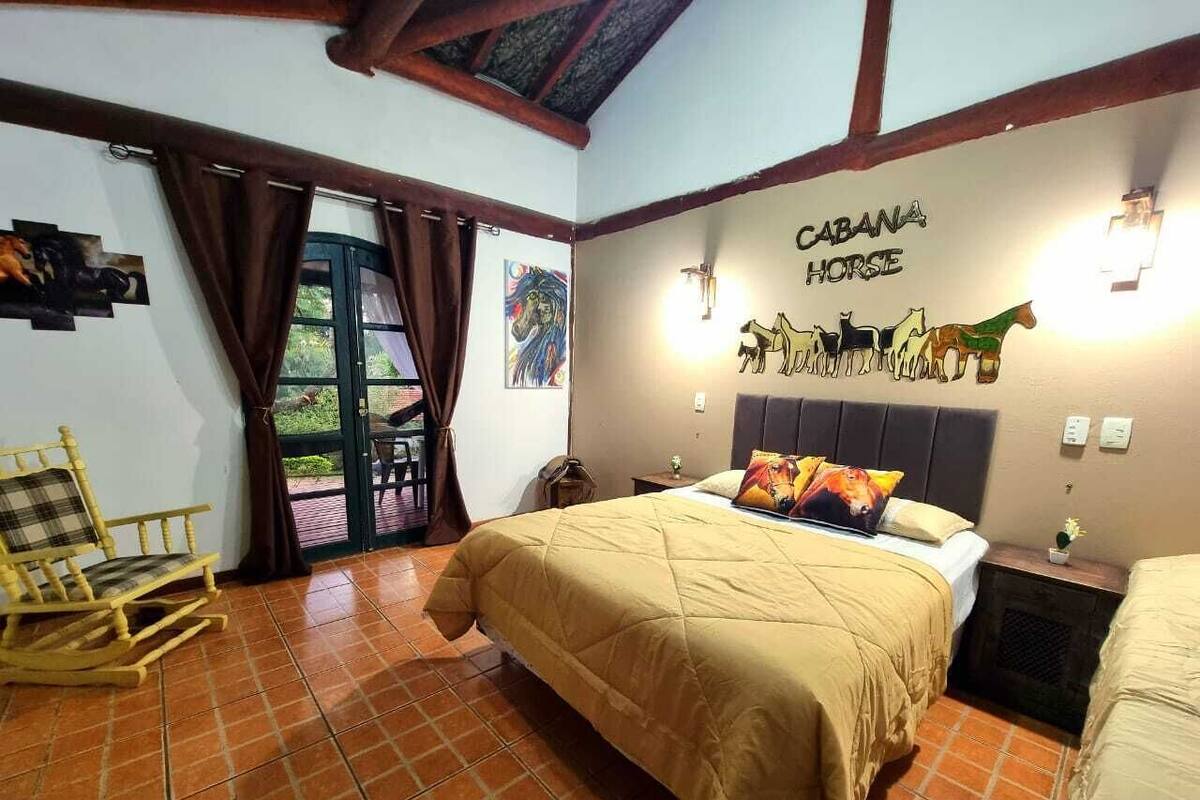 Un dormitorio con una cama, un sillón mecedor, un balcón con cortinas y una pared decorada con un letrero de caballos.