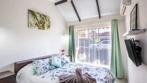 A bedroom with a bed, a window with curtains, a wall-mounted TV, and a painting. - Jaco Condo - Walk to beach! (Jaco)