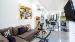 A modern living room with a sofa, a glass coffee table, and a painting on the wall. - Jaco Condo - Walk to beach! (Jaco)