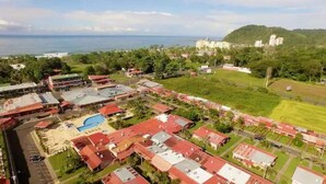 An aerial view of a residential area with multiple buildings, a swimming pool, and a view of the ocean. - Jaco Condo - Walk to beach! (Jaco)