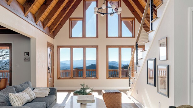 Un salon spacieux avec un plafond haut, de grandes fenêtres et une vue sur les montagnes.