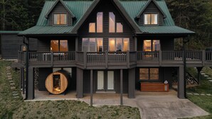 Une cabane en rondins à deux étages, dotée d’un balcon, d’une grande cuve en bois et d’un escalier en pierre.